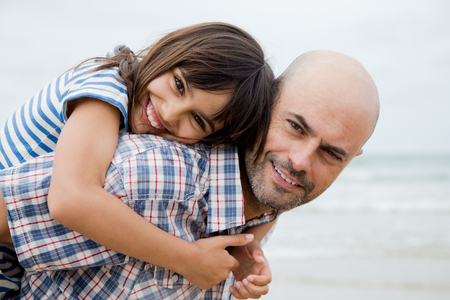 Father giving his daughter a piggy back ride on the beach in a cloudy dayの写真素材