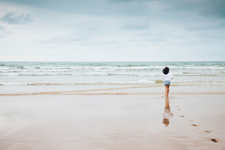 Girl running to the waves on the beach leaving the trace of her footsteps on the sand in a cloudy dayの写真素材