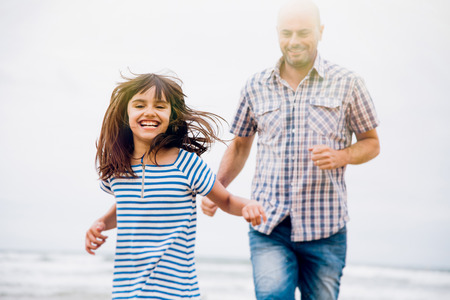 Father and daughter having fun playing tag on the beach in a cloudy day. Light effect added.の写真素材