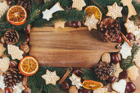 Wooden cutting board surrounded by fir branches, dry orange, cinnamon sticks, nuts, cookies and pinecones. Christmas cooking conceptの写真素材
