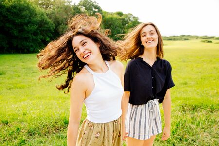 Two funny female friends turning heads to camera laughing and moving hair in the countryside