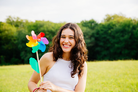 Cheerful and beautiful young woman holding a windmill toy in a green landscapeの写真素材