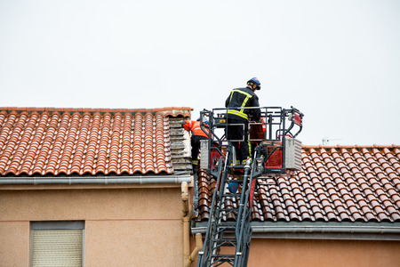 Firemen up in a crane removing detached tiles from a roof in a windy and rainy dayの写真素材