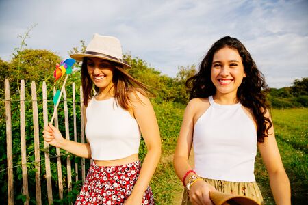 Funny female friends walking in the fields with hats and windmill in summerの写真素材