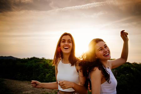Happy and funny female friends dancing on a cliff at sunset. Sun flareの写真素材