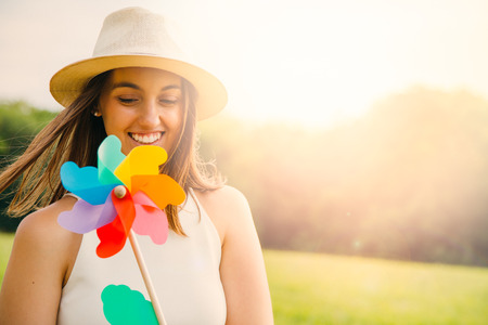 Happy cute young woman with hat walking holding a windmill toy outdoors in summer. Sun flare effectの写真素材