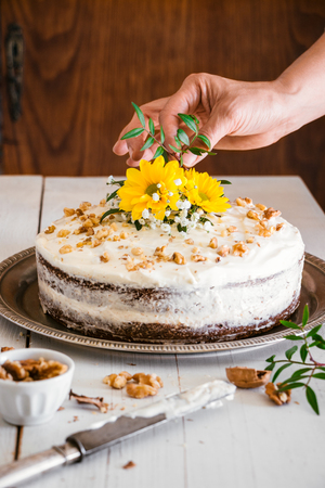Woman hand putting natural flowers on a naked carrot cakeの写真素材