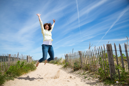 Happy middle aged woman jumping on the beach crazy for vacationの写真素材