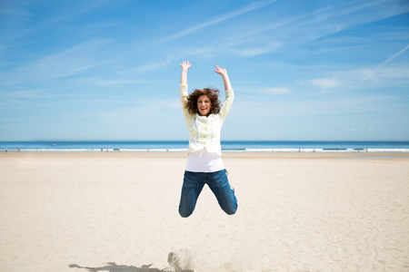 Happy midlde aged woman jumping on the beach crazy for vacationの写真素材