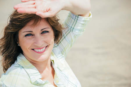 Beautiful middle aged woman protecting face from sun with hand on the beachの写真素材