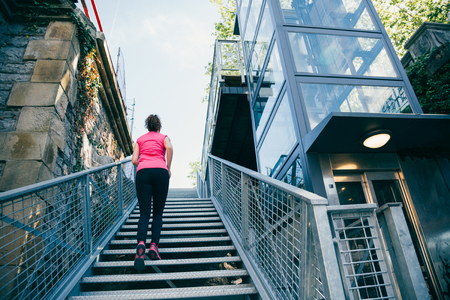 Middle aged woman climbing metallic stairs fast next to a elevator outdoors