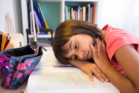 Exhausted school girl doing homework at homeの写真素材