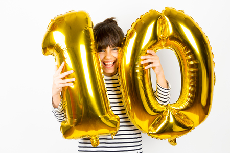 Happy little girl holding two golden balloons making the 10 number on white background. 10th anniversary celebration party.の写真素材