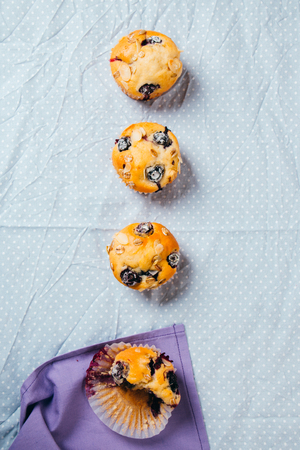 Freshly baked blueberry muffins with almond, oats and icing sugar topping in a row on a polka dots tablecloth. Top view.の写真素材