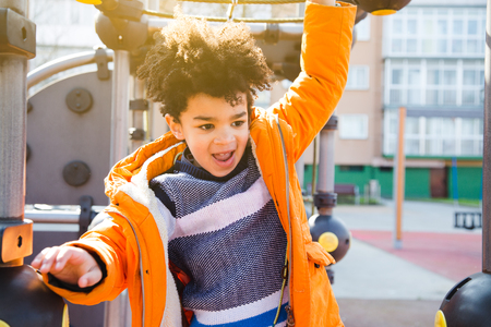 Happy kid in orange coat climbing on the playground in a sunny dayの写真素材