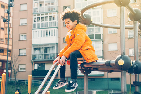 Happy kid in orange coat climbing on the playground in a sunny dayの写真素材