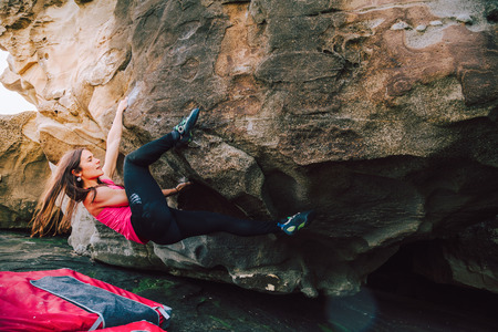 Young rock climber woman on a cliff rock at the coast with safety matsの写真素材
