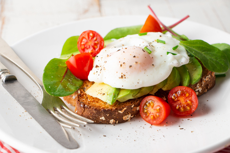 Healthy whole grain bread toast with avocado, poached egg, cherry tomato and baby leaves saladの写真素材