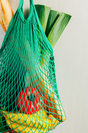 Green string shopping bag with vegetables, fruits and bread hanging on a hook in the kitchen. Close up.の写真素材