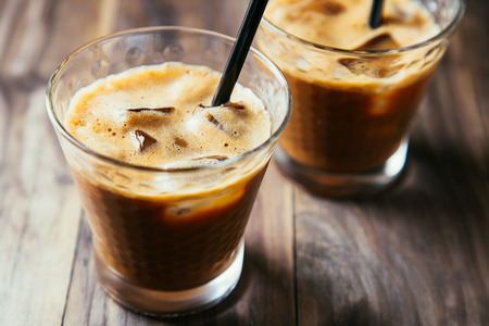 Two glasses of iced coffee latte with straws on a rustic wooden table