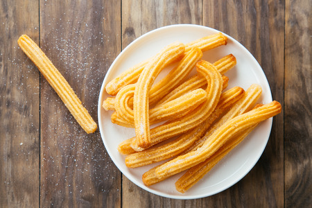 Traditional spanish churros with sugar in a white dish on a rustic wooden table. Top viewの写真素材