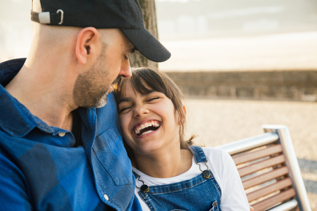 Father and daughter sitting on a bench on the waterfront having fun together in a sunny dayの写真素材