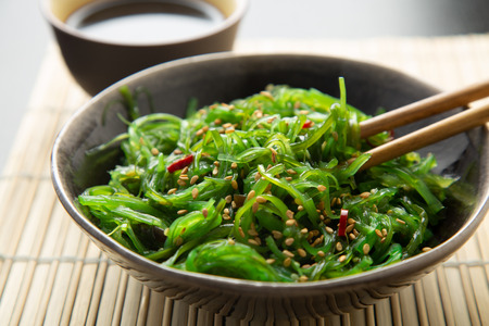 Wakame seaweed salad with sesame seeds and chili pepper in a bowl on a bamboo matの写真素材