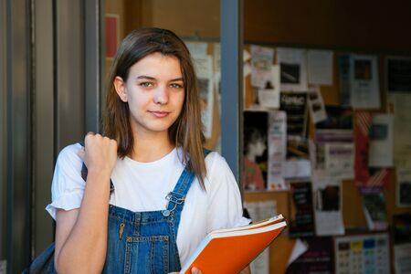 Portrait of a beautiful student girl at the school entrance with bulletin board at the backgroundの写真素材