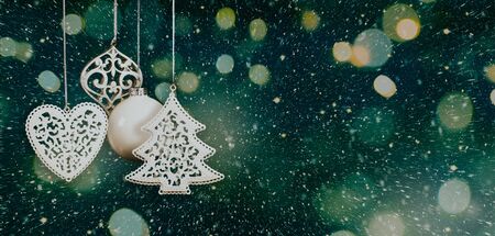 Hanging white Christmas baubles in a nordic style with blurred lights, sparks and snow on a dark greenish blue background. Copy spaceの写真素材