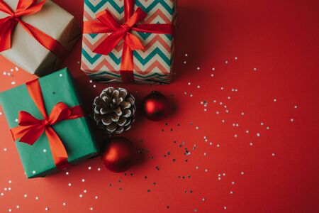Christmas gift boxes with pine cone, ornaments and star shaped glitter on a red background. Flat layの写真素材