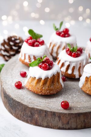 Small Christmas bundt cakes with sugar glaze and  currants on a rustic wood slice with Christmas lights on the backgroundの写真素材