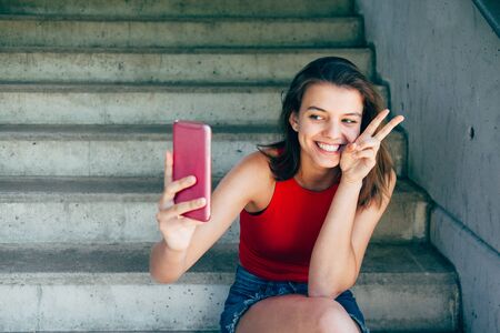 Cute teen girl taking a funny selfie sitting on the stairs