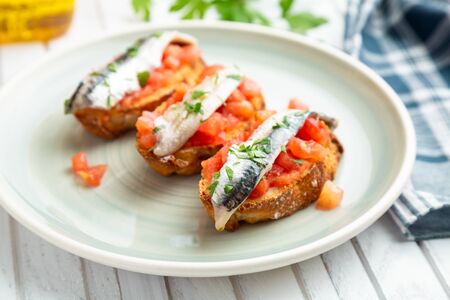 Delicious spanish tapa with marinated anchovies in vinegar, fresh tomato, olive oil and parsley on...