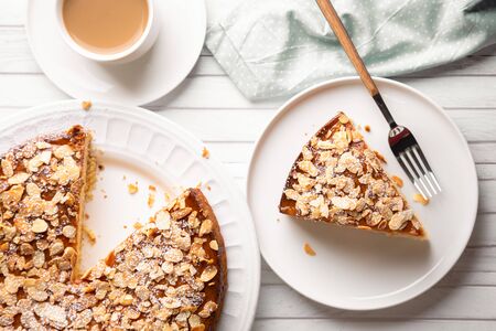 Almond and lemon cake with sliced almonds topping and a coffee cup on a white wooden table. Top view
