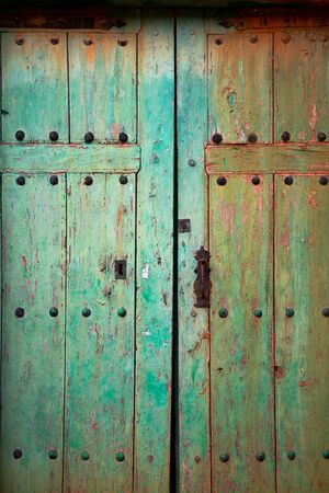Old rustic wooden door with different layers of cracked paint in green and orange colorsの写真素材