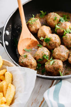 Meatballs in onion sauce with parsley in a frying pan and friesの写真素材