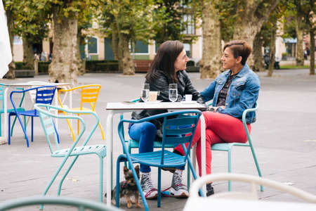 Middle aged lesbian couple with their yorkshire terrier having a coffee in a cafe terraceの写真素材