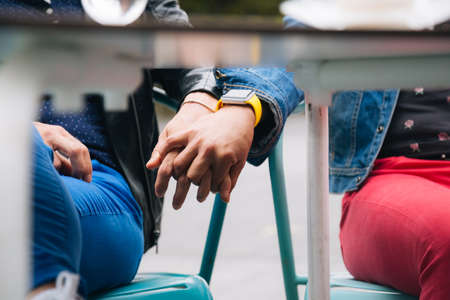 Unrecognizable lesbian couple holding hands under the table in a cafe terraceの写真素材
