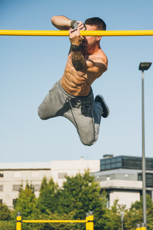 Young athletic man doing gymnastics with twirls on bars at a calisthenics gym outdoors