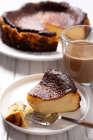 Traditional basque burnt cheesecake with a cup of coffee on a white wooden table.