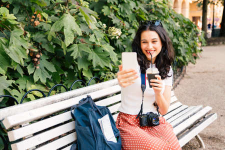 Young beautiful tourist woman with an ice coffee taking a selfie for her followers