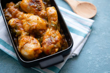 Chicken legs stewed with vegetables in a black casserole on a blue rough  surfaceの写真素材