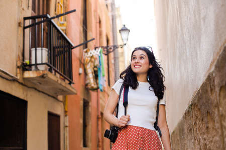 Young happy tourist woman walking down an european city alley with a vintage cameraの写真素材
