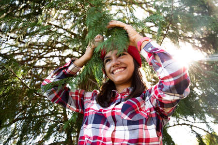 Happy teen girl hiker playing with branches of a pine tree with the sun behind in autumn. Happy to be in contact with natureの写真素材