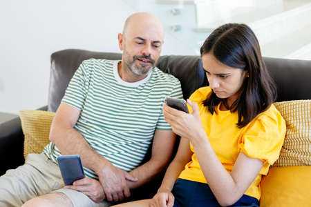 Father peeking what his teen daughter is watching in her smart phone. Parental control concept. Focus on herの写真素材