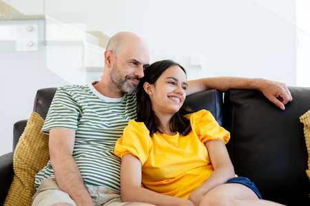 Happy father and teenage daughter sharing relaxing moments sitting in the sofa at homeの写真素材