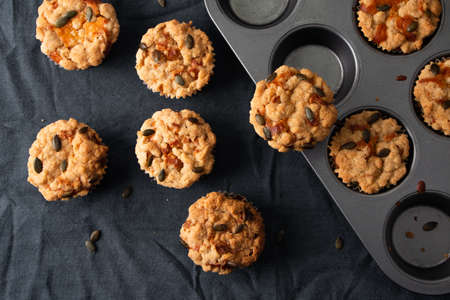 Pumpkin muffins with crumble and seeds topping in a muffin tin on a dark clothの写真素材