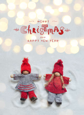 Christmas greeting card with little Christmas dolls ornaments making angels in the snow with lights bokeh. Funny handwriting letteringの写真素材