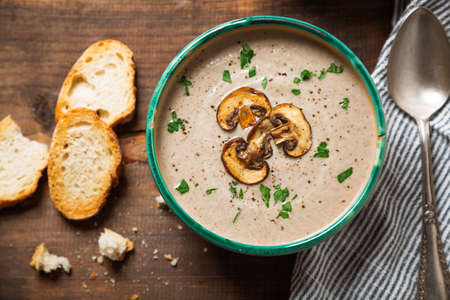 Homemade creamy mushroom soup with sliced mushrooms topping in an old bowl and bread toast on a rustic wooden tableの写真素材