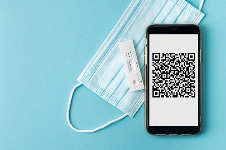 Smartphone with generic vaccination QR code, negative rapid test card and surgical mask on a blue backgroundの写真素材